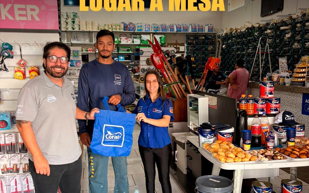 Capa do registro do Dia do Pintor na Construind, em Minas Gerais: participantes ao lado da mesa de café e de materiais Coral. Texto: Quem faz a obra acontecer merece lugar à mesa.